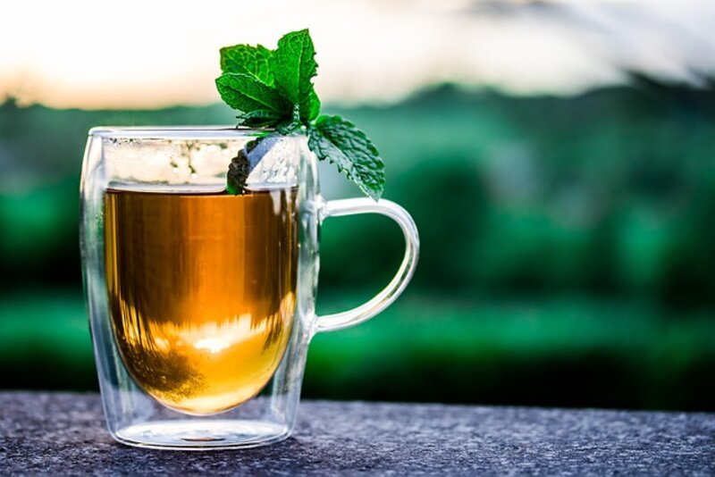 Steaming cup of calming herbal tea with dried herbs and flowers surrounding it